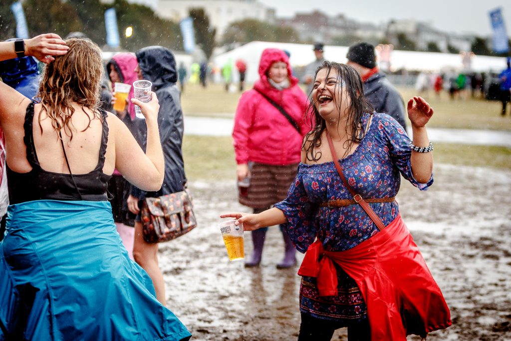 Festival goers dancing in the mud looking very wet from the rain but with big smiles and holding pints