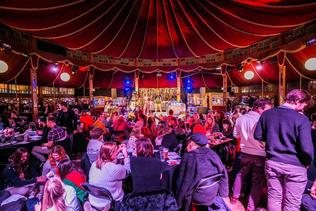 The view looking at the stage of the Spiegeltent, with the middle floor hosting round table of people, and the magnificent circus-style roof showcasing the round tent at Winterville