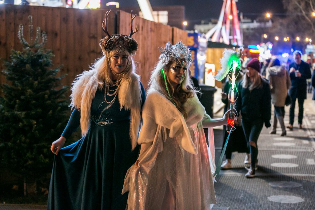 Two ladies dressed as winter fairies/goddesses, wearing velvet dresses, headdresses and fur collars.