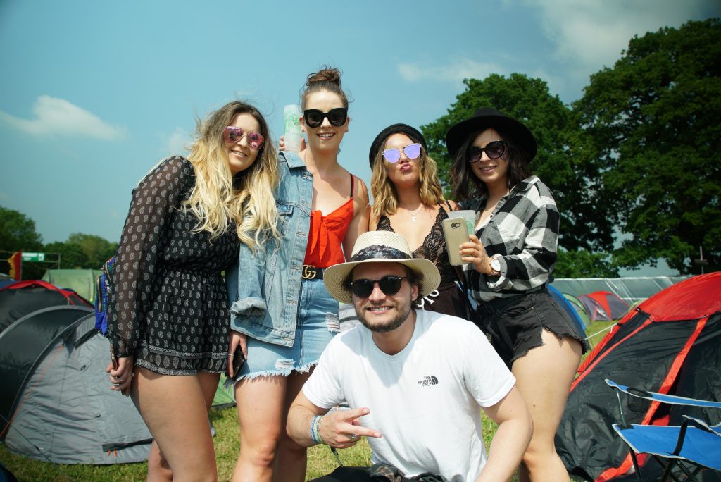 Group of festival goers smiling in the Under The Hill festival campsite in 2018. 5 festival friends in the sunshine amongst the tents!