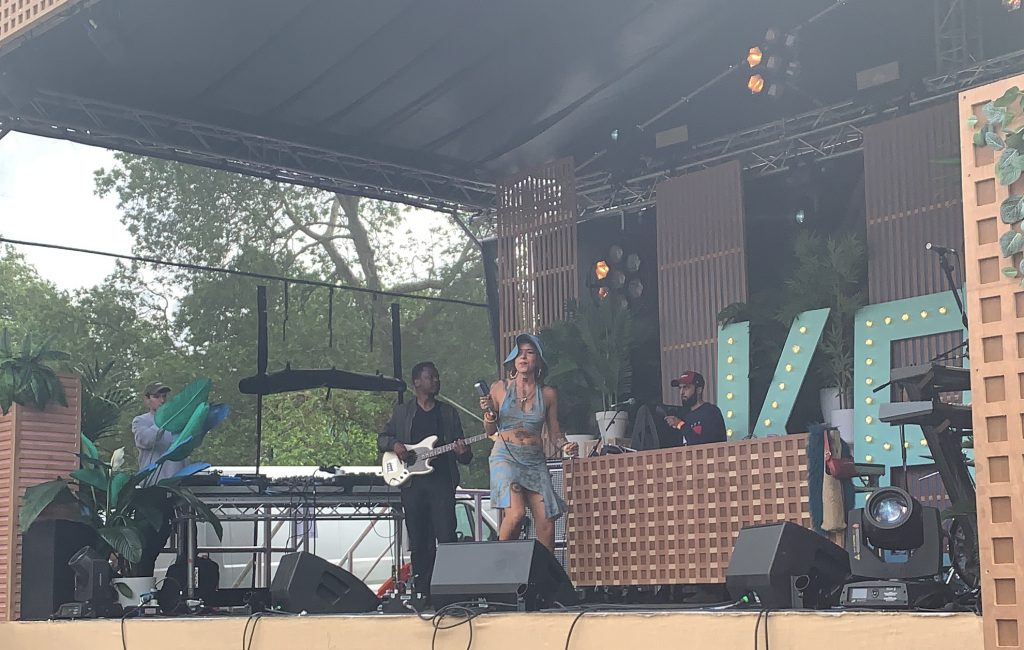 Greentea Pend on the main stage at Jam On Rye Festival wearing a blue floppy hat and matching blue top & skirt. She's clearly loving life, dancing while singing.