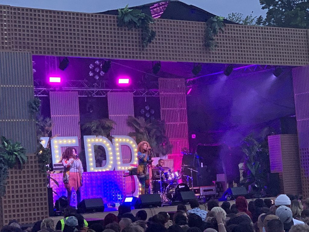 Kelis grips the microphone on the main stage in her incredible catsuit, lit up by pink and purple lights as the sun goes down.