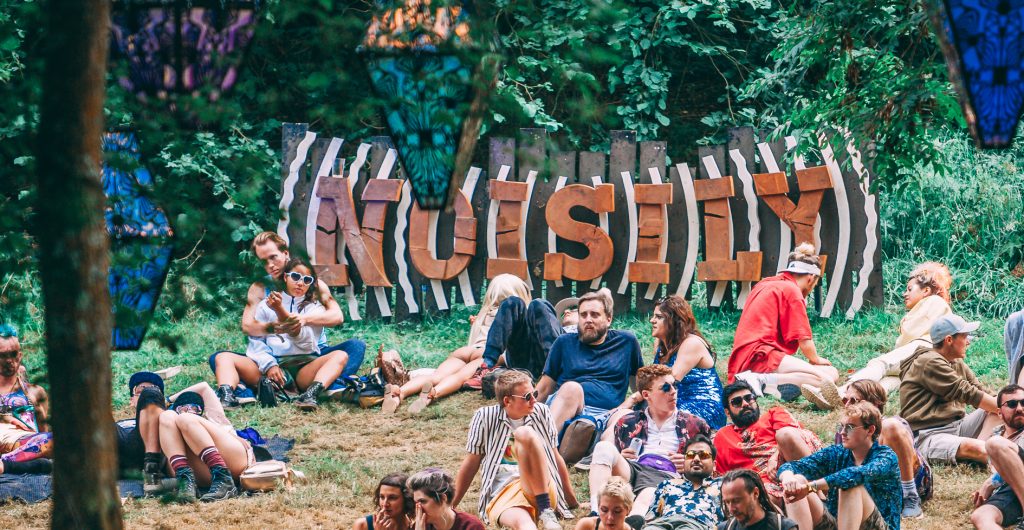 The Noisily Festival 2019 sign above a group of people chilling. The whole place lit up at night!