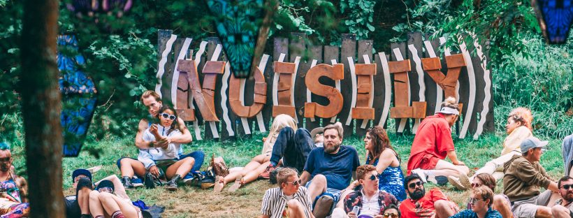 The Noisily Festival 2019 sign above a group of people chilling. The whole place lit up at night!