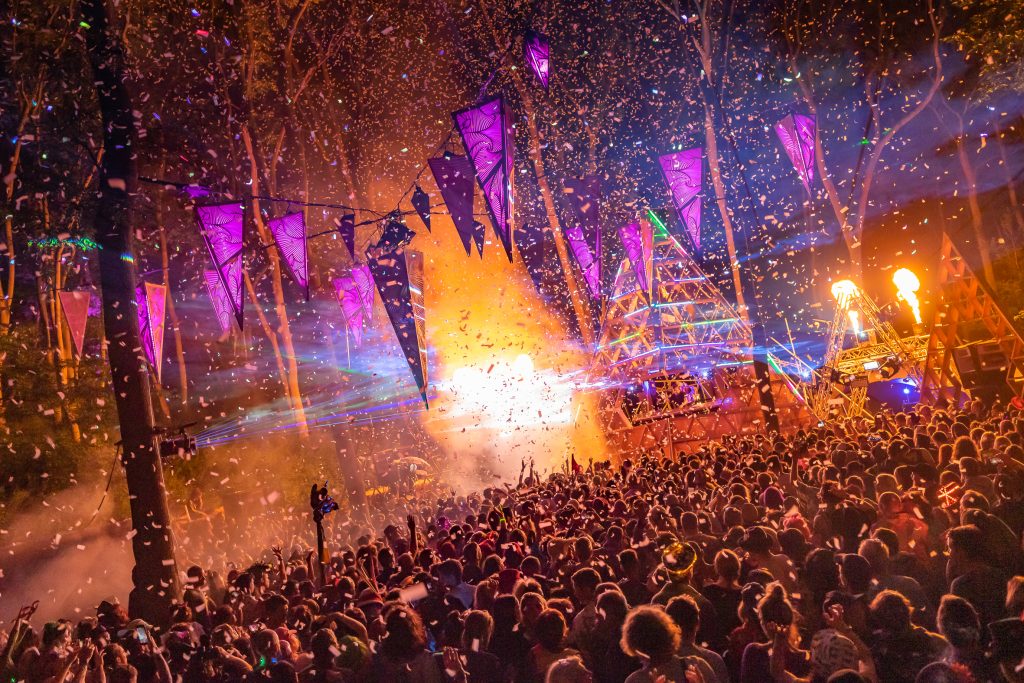 Confetti over the Noisily stage (which is consider the main stage). Flames burst from behind the wooden stage, lots of people are dancing in front, and there are triangle LED lights hanging over the crowd at Noisily Festival 2019