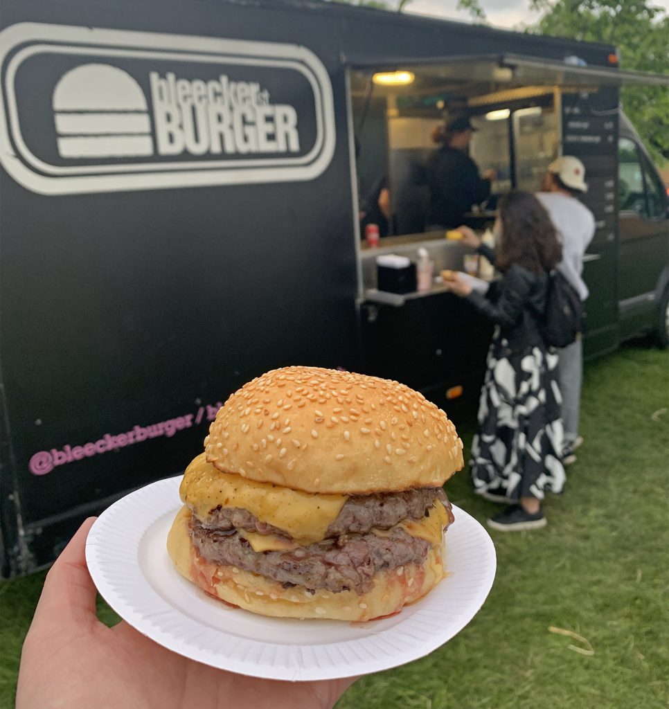 The focus is on my Bleecker double cheeseburger which is juicy and covered in melted cheese. In the blurred background is the monochrome Bleecker Burger truck. Bleecker were one of two 'headline food' acts at Jam on Rye Festival 2019
