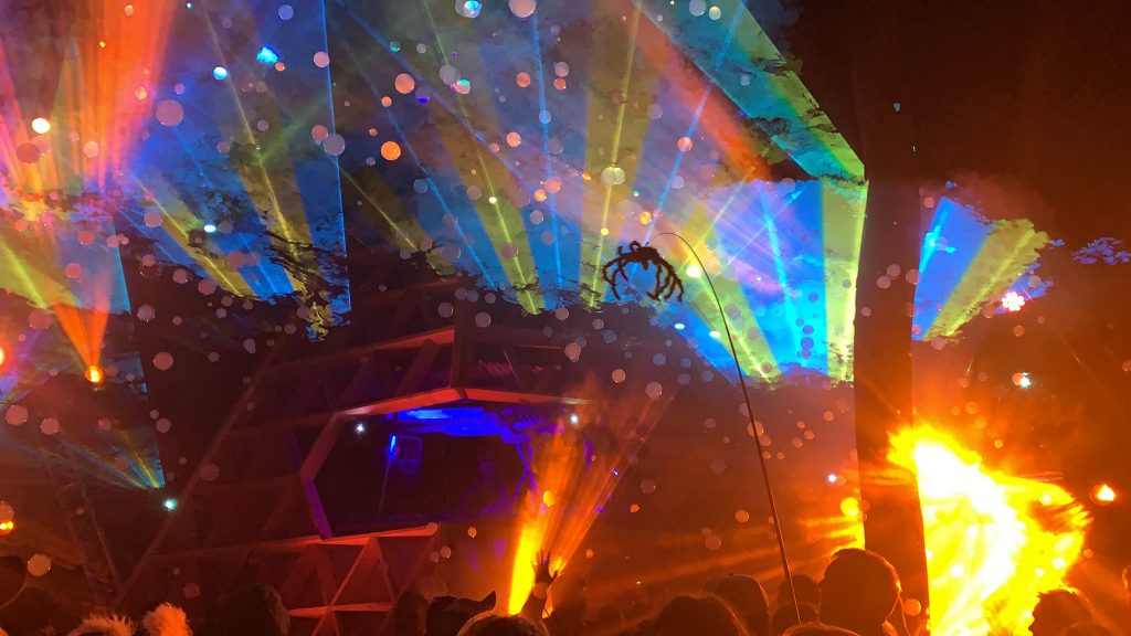 Blue and green lasers illuminate the smoky air in front of the Noisily Stage creating amazing patterns. There are smoke filled bubbles floating too and someone has a big fake furry spider dangling from a stick.