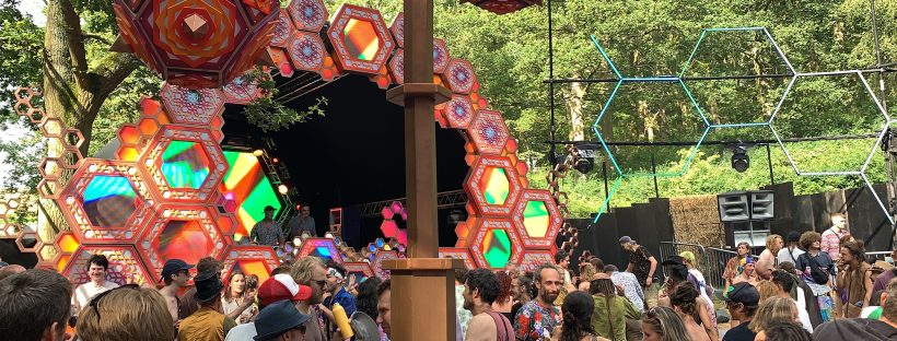 The Liquid Stage (psytrance stage) is designed with lots of hexagon shapes in orange, red and purple. The crowd are all happily dancing in the daytime!
