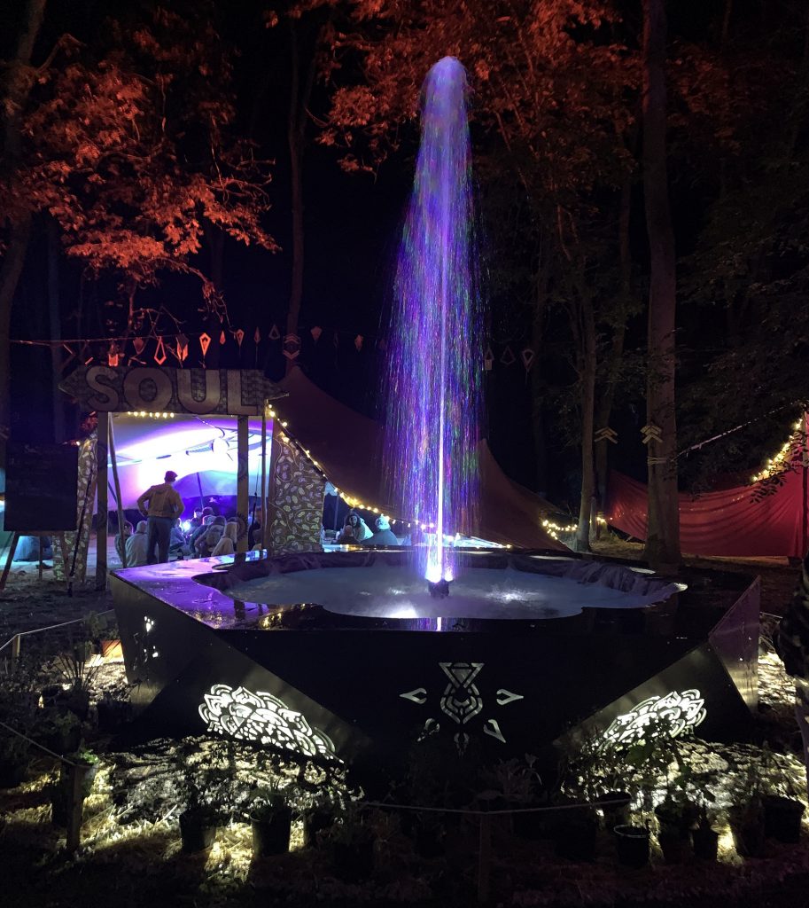 A large fountain that is illuminated with coloured LED lights both in the spray of the fountain and underneath the bowl