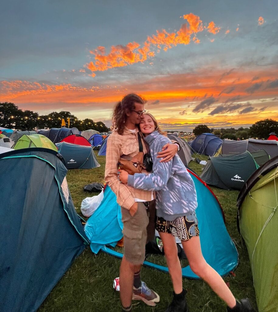 Henri and Ell share a cuddle stood between the tents in the Nozstock campsite with a gorgeous orange cloud sunset behind them